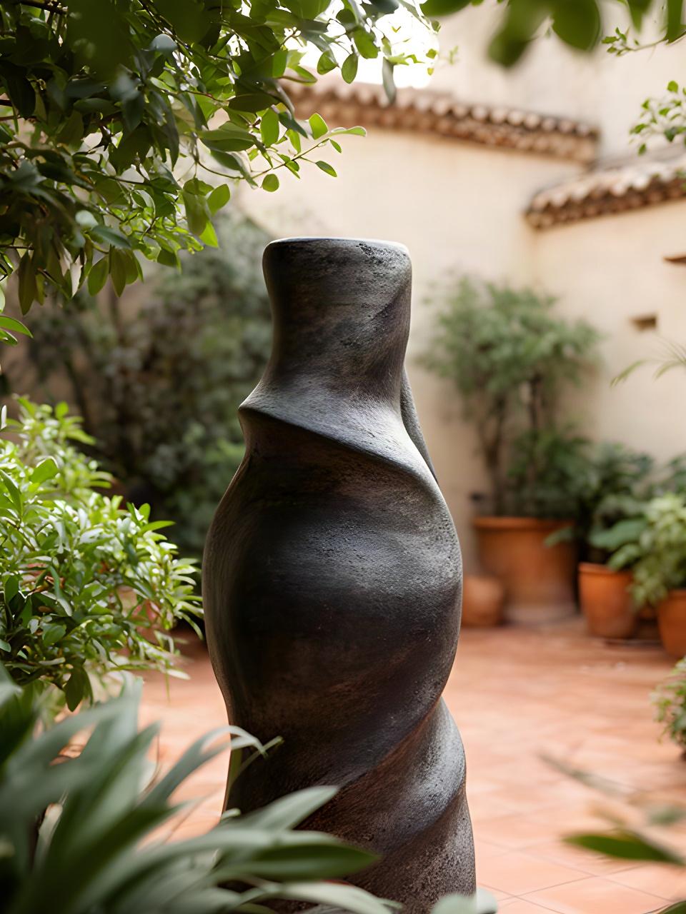 Scultura contemporanea in gres dalle forme organiche esposta tra piante in un cortile luminoso